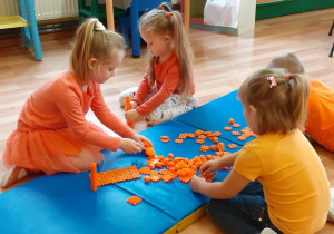 4 dzieci buduje z pomarańczowych klocków.